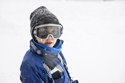 Portrait of boy wearing ski goggles while standing on snow covered field