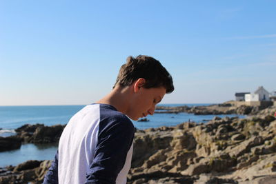 Side view of boy standing at beach against clear blue sky