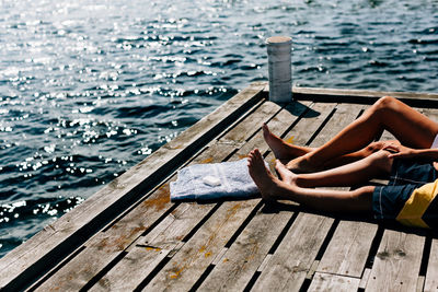 Low section of friends relaxing on pier by sea during sunny day