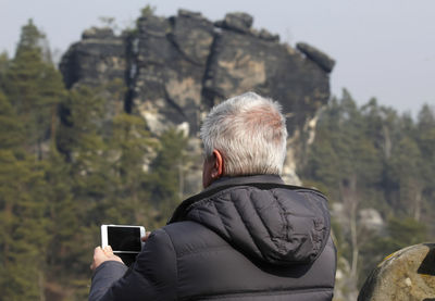 Rear view of man photographing with mobile phone