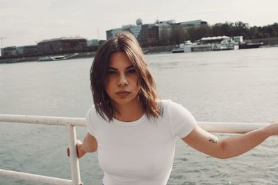 Portrait of beautiful woman standing by railing against sea