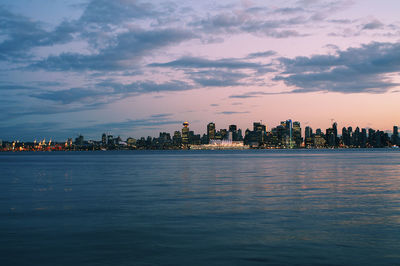 Sea by illuminated buildings against sky during sunset