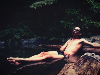 Young man looking away while sitting by tree against plants