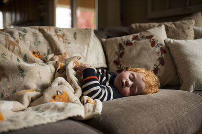 Young boy sleeping on couch at home under warm blanket