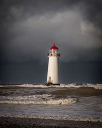 Lighthouse by sea against sky during sunset