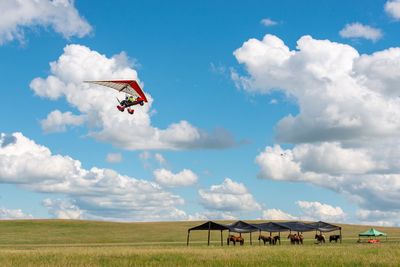 Man hang gliding over field against sky