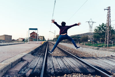 Rear view of teenage girl jumping over railroad tracks against clear sky