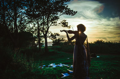 Woman standing in front of tree at sunset