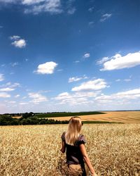 Rear view of woman walking on dry wheat farm against sky