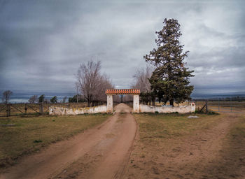 Country road with trees against cloudy sky