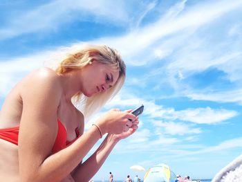 Side view of woman using mobile phone against sky