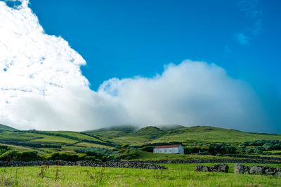 Scenic view of green landscape and hills against cloudy sky