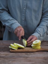 Closeup adult woman hands cutting fresh green apples on wooden cutting board 