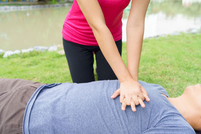 Midsection of woman giving cpr to man lying in grassy field