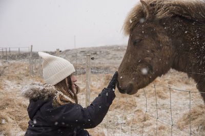 Smiling woman touching horse on field during winter