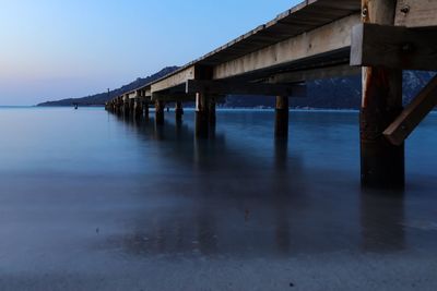 Pier over river against sky during sunset