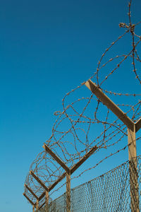 Low angle view of chainlink fence against clear blue sky