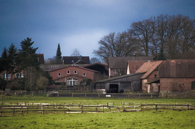Barn on field by houses against sky