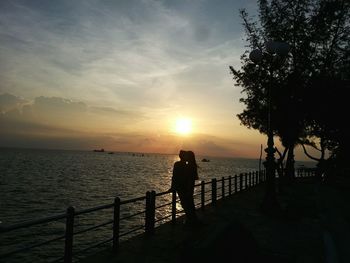 Silhouette man standing on railing against sea during sunset