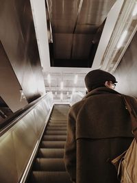 Rear view of man standing on escalator in building