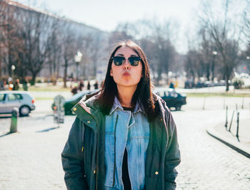 Young woman in sunglasses puckering lips while standing on city street