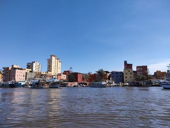 River and buildings against clear blue sky