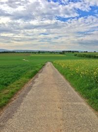 Road passing through field against cloudy sky