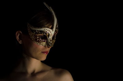 Topless woman wearing carnival mask against black background