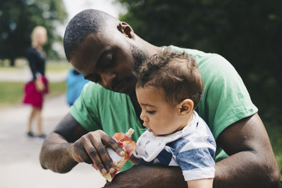 Father feeding son while sitting at park
