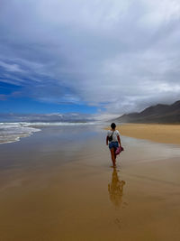Rear view of woman walking at beach against sky