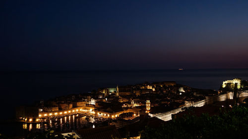 High angle view of illuminated city by sea against sky at night