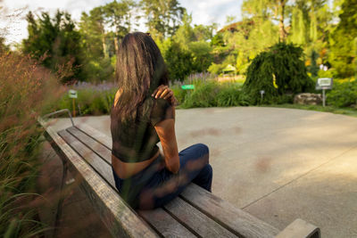 Rear view of woman sitting on park bench in public park