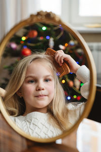 A cute 8-year-old girl looks into the reflection of the mirror and combs her hair.