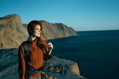 Woman standing on rock by sea against sky