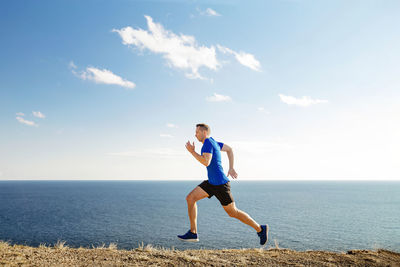 Full length of woman exercising at beach against sky