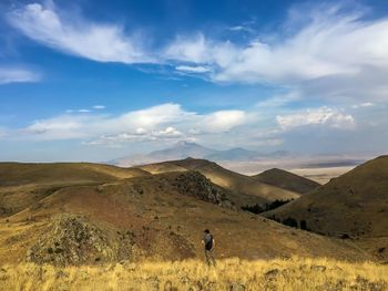 Rear view of man standing on landscape against cloudy sky