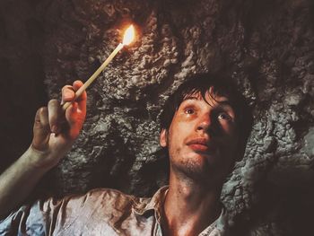 Close-up of man holding illuminated candle while standing in cave
