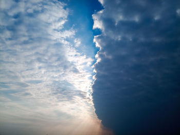 Low angle view of sunlight streaming through clouds