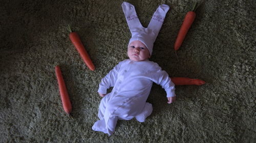 Portrait of baby girl with carrots lying down on rug