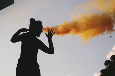 Young woman holding distress flare against sky