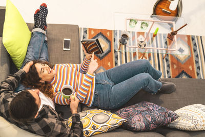 High angle view of happy woman lying on boyfriend lap at home