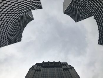 Directly below shot of buildings against cloudy sky in city