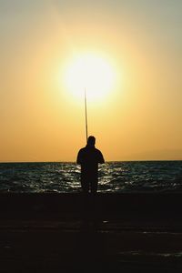 Rear view of silhouette man fishing in sea during sunset