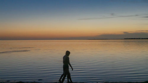 Silhouette boy standing on beach against sky during sunset