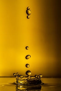 Close-up of drop falling in water against orange background