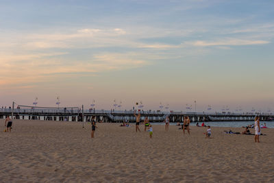 Group of people on beach against sky during sunset