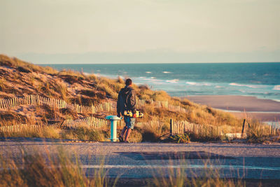 Rear view of man riding on sea shore against sky