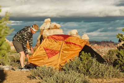 Camper in camo windbreaker finishes setting up tent in utah desert