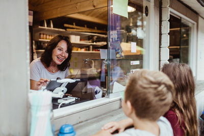 Smiling woman taking order from siblings standing by concession stand