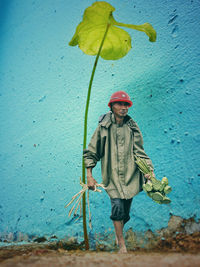 Senior man holding plants while standing on street against blue wall